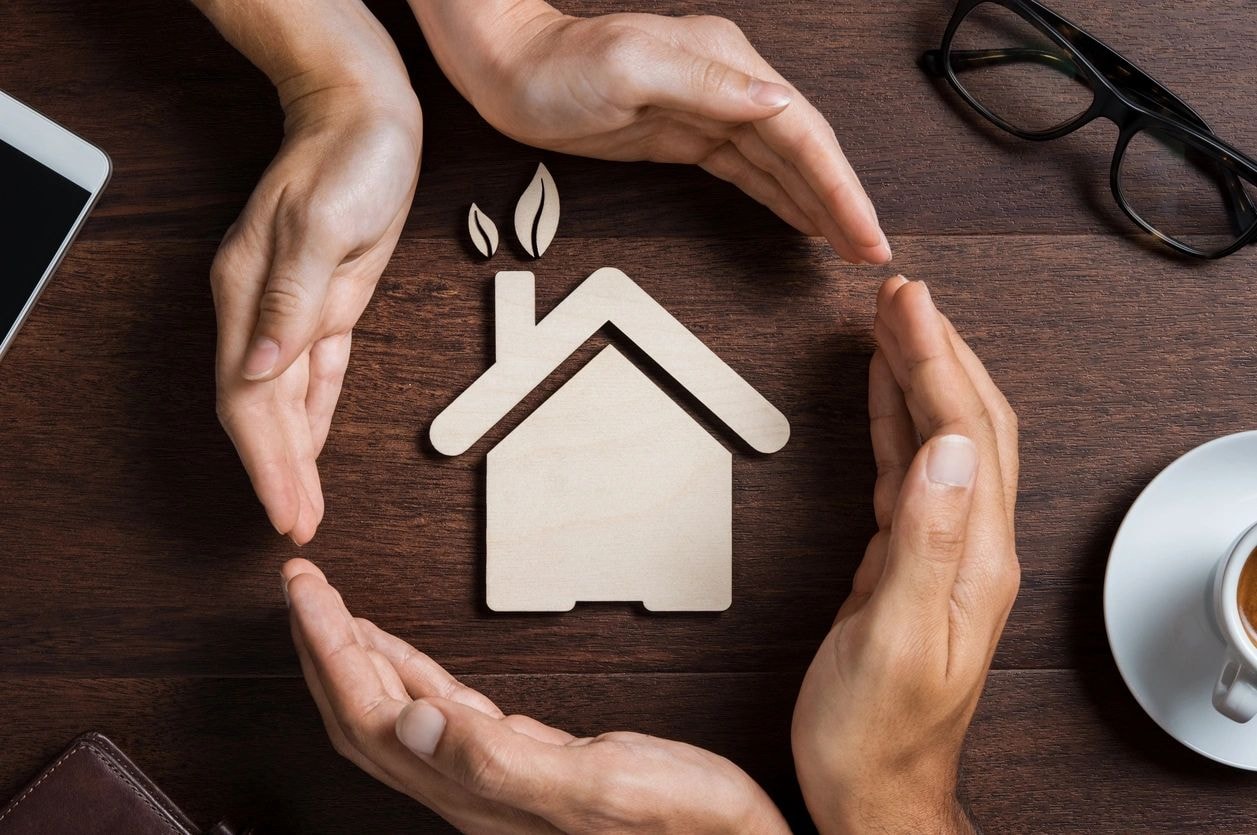 Hands protecting a paper house representing home care and rental stability